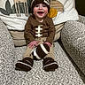 Cooper is registered to the contest to win money with this photo: baby, child, smiling, knit_hat, football_toy, brown_clothing, armchair, cushion, animal_pillow, indoor, happy, sitting, cozy, textured_fabric, cute, playful, young_child, headwear, toy, portrait