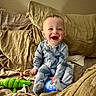 baby, child, pajamas, bed, pillows, toy, crocodile_toy, pacifier, happy, smiling, indoor, cozy, cute, infant, person, playful, glowing_device, soft_furniture, home, relaxed