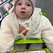 éléa participe au concours pour gagner de l'argent avec cette photo : baby, child, shopping_cart, jacket, hat, blue_eyes, grocery_store, aisle, shopping, winter_clothing, curious, face, person, infant, indoor, clothing, wool, warm, seat, portrait