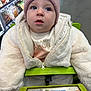 baby, child, shopping_cart, jacket, hat, blue_eyes, grocery_store, aisle, shopping, winter_clothing, curious, face, person, infant, indoor, clothing, wool, warm, seat, portrait