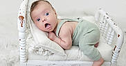 Bennett joined the competition — help win amazing prizes! baby, infant, green_romper, small_bed, white_bed, wooden_bed, fluffy_rug, surprised_expression, wide_eyes, open_mouth, cushion, knitted_blanket, indoor, portrait, cute, child, resting, soft_lighting, white_background, cozy