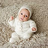 Bennett is registered to the contest to win money with this photo: baby, infant, knitted_clothing, white_outfit, bonnet, blanket, fluffy, soft_texture, cute, portrait, child, newborn, lying_down, cozy, warm, small_hands, wide_eyes, pout, indoor, neutral_colors