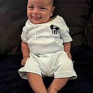 Frankko is registered to the contest to win money with this photo: baby, smiling, tongue_out, mickey_mouse, blue_outfit, necklace, bracelet, couch, dark_background, sitting, happy, infant, cute, indoors, person, child, comfortable, plush, casual_clothing, portrait