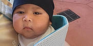 Alex is registered to the contest to win money with this photo: baby, child, face, beanie, black_hat, baby_carrier, hand, outdoor, pavement, drain, clothing, cute, expressionless, person, young_child, closeup, infant, headwear, soft_texture, skin
