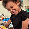 child, toddler, smiling, winking, black_tshirt, indoor, hair, happy, playing, table, chair, toy, colorful, person, face, cute, expression, young, skin, casual