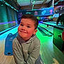 bowling_alley, bowling_ball, bowling_lane, boy, casual_clothing, child, colorful, fun, happy, hoodie, indoor, leisure, neon_lights, person, playful, recreation, smiling, sport, wooden_floor, young