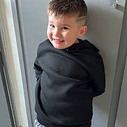 Eden a rejoint le concours — aidez-le/la à gagner de superbes lots ! child, boy, smiling, black_hoodie, camo_pants, short_hair, haircut, indoor, door, floor, happy, standing, casual_clothing, portrait, young, person, cute, fashion, trendy, wall