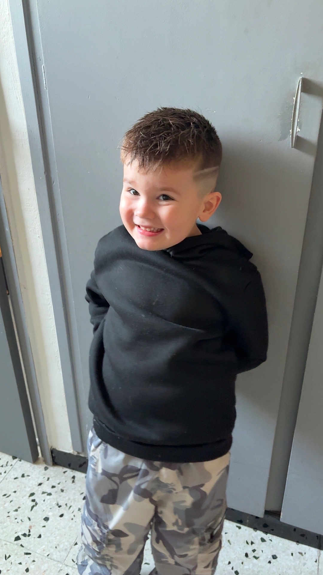 Eden a rejoint le concours — aidez-le/la à gagner de superbes lots ! child, boy, smiling, black_hoodie, camo_pants, short_hair, haircut, indoor, door, floor, happy, standing, casual_clothing, portrait, young, person, cute, fashion, trendy, wall