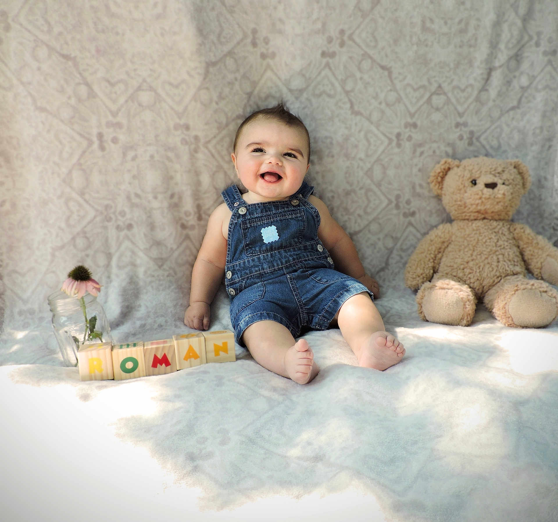 Roman is registered to the contest to win money with this photo: baby, denim_overalls, smiling, teddy_bear, blocks, flower, jar, blanket, patterned_background, happy, child, sitting, indoor, cute, playful, toys, portrait, infant, soft_light, cozy