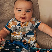 Roman is registered to the contest to win money with this photo: baby, child, smiling, couch, onesie, animal_print, comic_book, colorful, indoor, happy, portrait, playful, infant, seated, cute, young_child, furniture, person, relaxed, bright