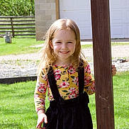 Lily joined the competition — help win amazing prizes! child, girl, smiling, outdoor, green_grass, wooden_post, flower_print, long_hair, sunlight, fence, garage, casual_clothing, happy, nature, daylight, person, standing, portrait, young_child, playful