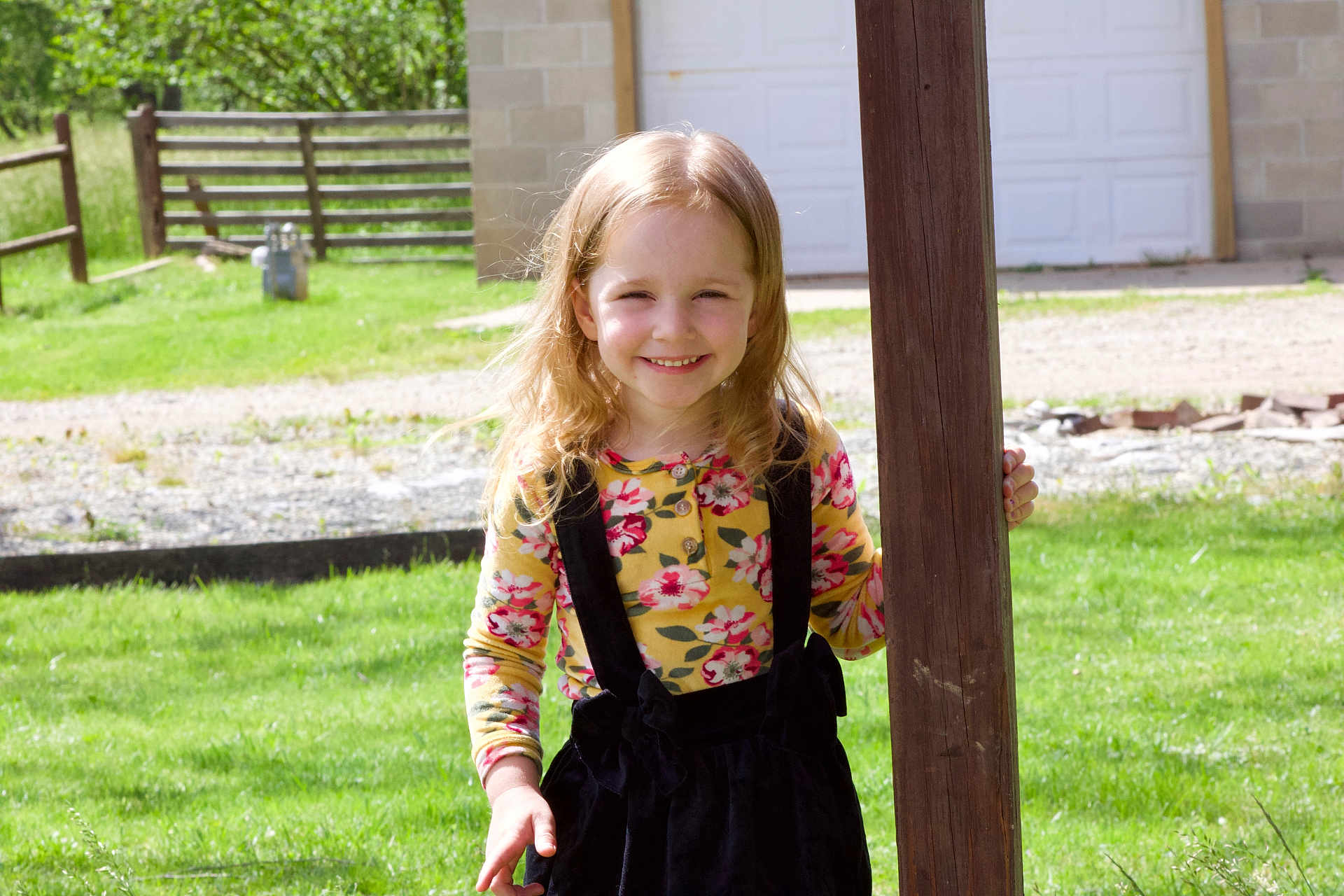 Lily joined the competition — help win amazing prizes! child, girl, smiling, outdoor, green_grass, wooden_post, flower_print, long_hair, sunlight, fence, garage, casual_clothing, happy, nature, daylight, person, standing, portrait, young_child, playful