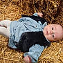 baby, infant, child, straw, hay, blue_clothing, vest, lying_down, curious, outdoor, soft_light, face, eyes, small_fingers, cute, warm_clothes, nature, texture, relaxing, portrait