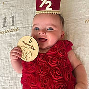 Adeline joined the competition — help win amazing prizes! baby, infant, child, red_dress, rose_pattern, milestone_card, crown, smiling, lying_down, blanket, happy, cute, portrait, hand, face, blue_eyes, skin, celebration, age_marker, indoors