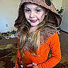 child, costume, orange_clothing, hood, face_paint, smile, blue_eyes, blonde_hair, long_hair, indoor, toy, play, person, happy, young, scarf, fabric, earring, portrait, home