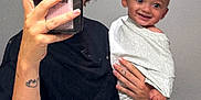 Enzo participe au concours pour gagner de l'argent avec cette photo : baby, person, mirror, selfie, smartphone, hand, tattoo, cloth, smile, face, arm, indoor, black_shirt, holding, baby_wrapped, short_hair, nail_polish, casual, background, grinning