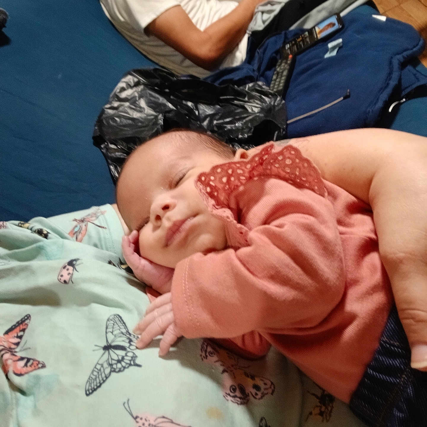 Ziya is registered to the contest to win money with this photo: adult, baby, blanket, blue_couch, butterfly_pattern, casual_clothing, comfort, face, furniture, hand, home, indoor, person, phone, pink_clothing, portrait, relaxing, rest, sleeping, wooden_floor