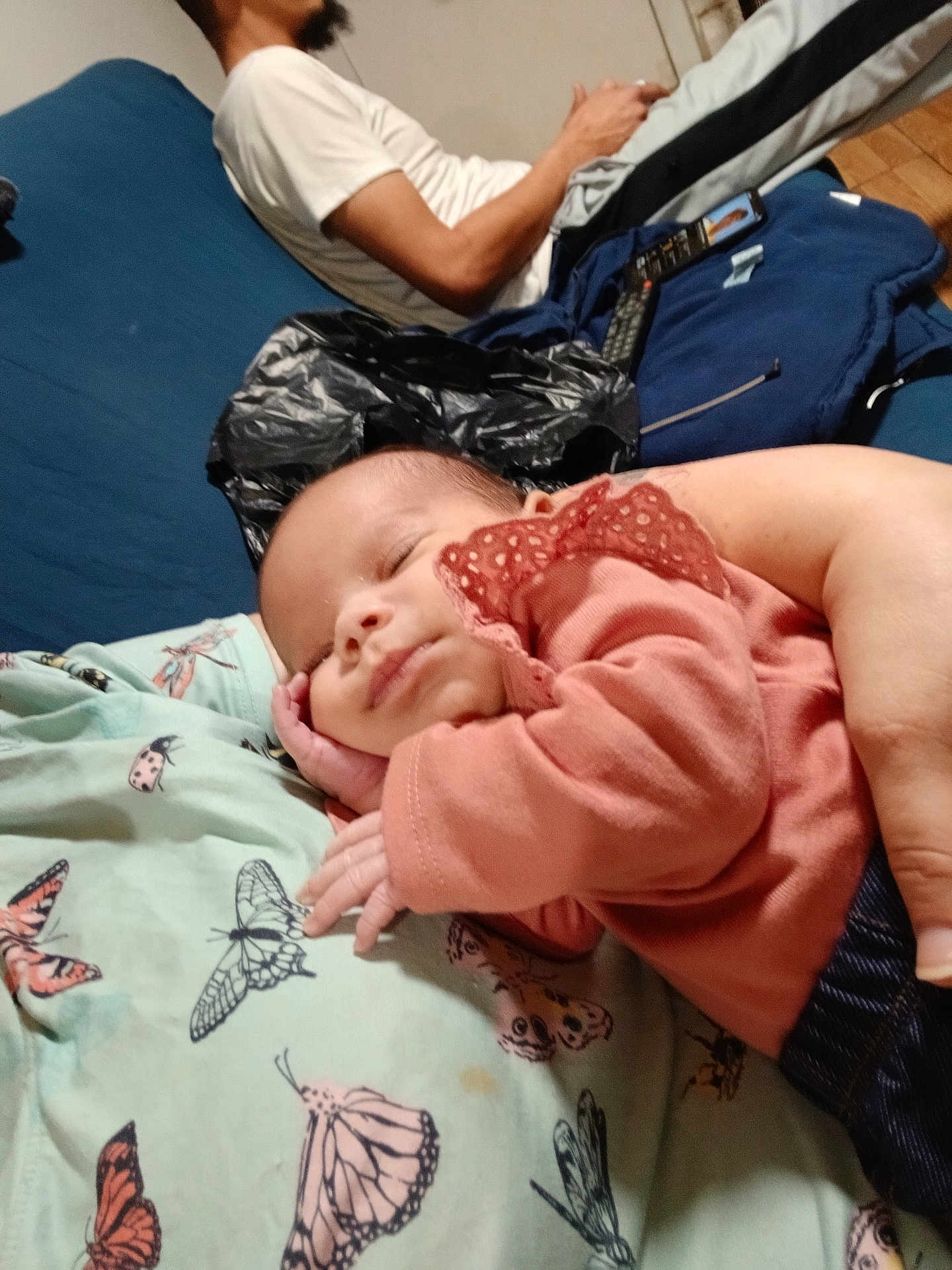 Ziya is registered to the contest to win money with this photo: baby, sleeping, pink_clothing, blanket, butterfly_pattern, adult, phone, casual_clothing, indoor, relaxing, hand, face, person, furniture, blue_couch, wooden_floor, comfort, rest, portrait, home