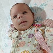 Ziya is registered to the contest to win money with this photo: baby, infant, floral_onesie, pacifier_clip, blanket, lying_down, curious_expression, soft_lighting, indoors, cute, small_hands, face, head, person, newborn, child, sleepwear, pattern, fabric, comfort