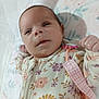baby, infant, floral_onesie, pacifier_clip, blanket, lying_down, curious_expression, soft_lighting, indoors, cute, small_hands, face, head, person, newborn, child, sleepwear, pattern, fabric, comfort