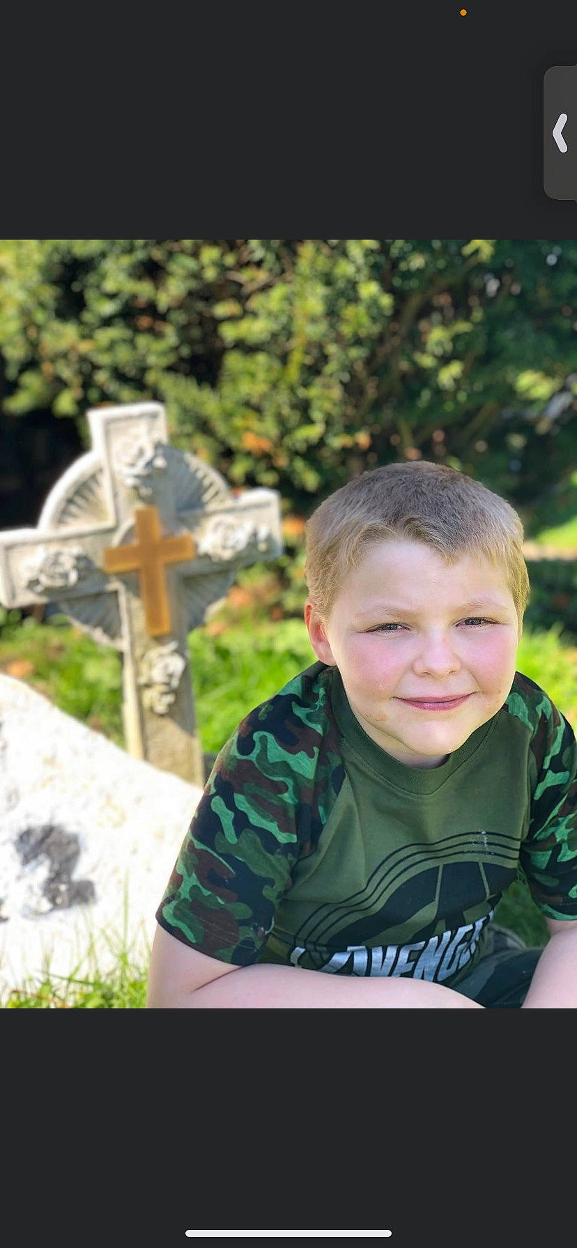 Aidan is registered to the contest to win money with this photo: cemetery, child, cross, flash_photography, fun, grass, grave, happy, headstone, joy, leisure, people_in_nature, person, plant, sitting, sleeve, smile, symbol, t_shirt, toddler