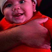 Kenny joined the competition — help win amazing prizes! baby, smile, face, hat, red_clothing, hand, adult, closeup, joyful, infant, warm_clothing, portrait, cute, skin, person, holding, headwear, expression, human, indoors