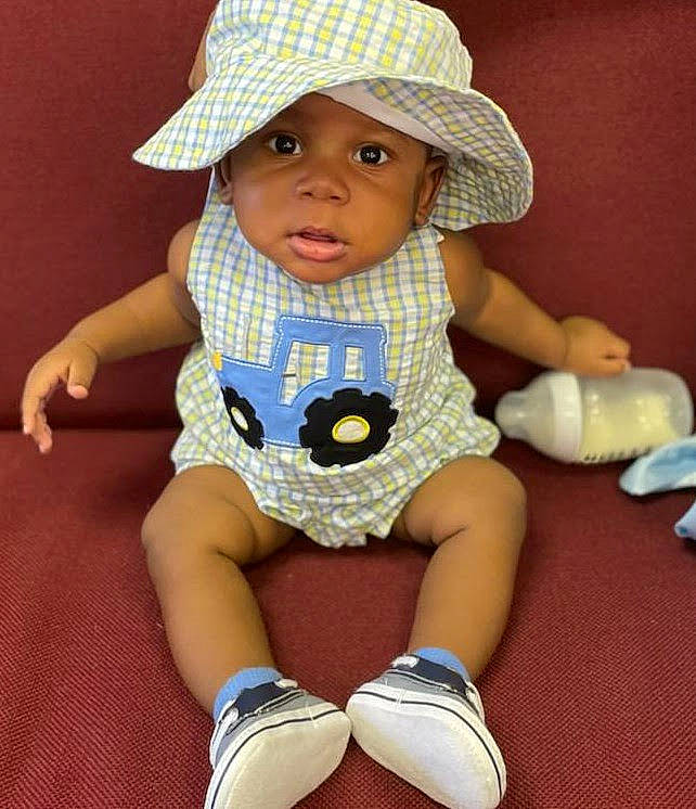 Devon is registered to the contest to win money with this photo: baby, baby_products, baby_toddler_clothing, cap, cheek, child, doll, electric_blue, fashion_accessory, hat, headwear, knee, pattern, person, sitting, skin, sleeve, sock, sun_hat, toddler