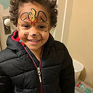 Kyle joined the competition — help win amazing prizes! child, face_paint, smile, curly_hair, jacket, black_jacket, indoor, door, zipper, happy, person, young_child, face, portrait, clothing, warm_clothing, curly_hair_child, fun, painted_face, expression