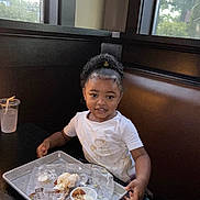 Eliyah joined the competition — help win amazing prizes! child, smiling, curly_hair, white_shirt, messy_shirt, restaurant, booth, tray, food_tray, sauce_cup, plastic_cup, table, window, daylight, indoor, person, seat, happy, curly_ponytail, eating