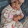 baby, bed, blanket, child, closeup, cozy, cute, eyes, face, floral_outfit, hands, indoors, infant, looking_at_camera, lying_down, photography, pink_bow, portrait, soft_texture, tongue