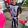 child, costume, skeleton, face_paint, outdoor, concrete, sidewalk, hose_reel, garden, toy, shoes, pink_tutu, dress_up, smiling, happy, playful, casual, daylight, person, yard