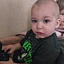 Jason joined the competition — help win amazing prizes! child, toddler, indoor, person, black_tshirt, green_text, sitting, curious, holding_object, short_hair, couch, background_child, casual_clothing, portrait, young, looking_at_camera, two_children, home, relaxed, furniture