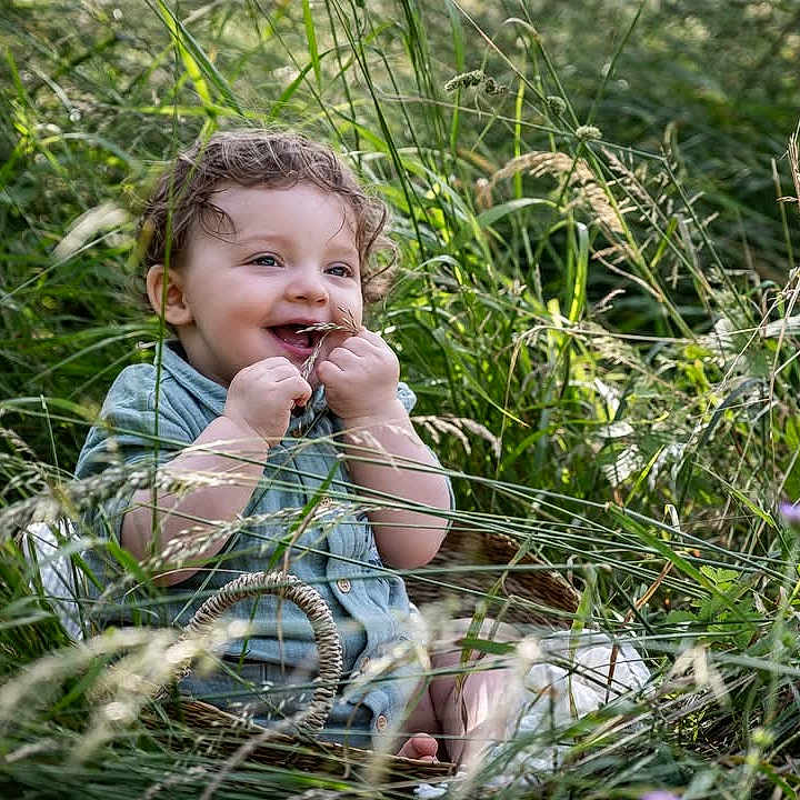 Tiago participe au concours pour gagner de l'argent avec cette photo : barefoot, basket, blades_of_grass, casual_clothing, child, curly_hair, cute, daylight, grass, greenery, happy, innocence, nature, outdoor, playful, portrait, sitting, smiling, summer, toddler