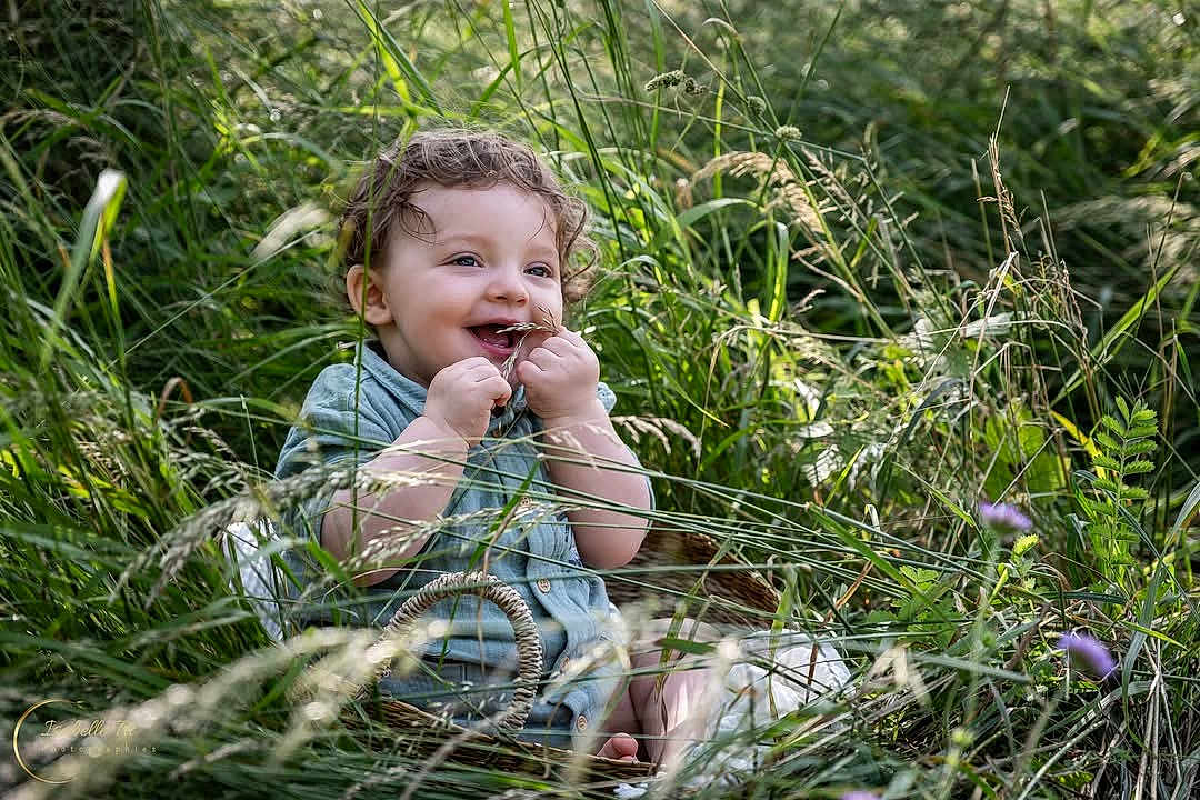 Tiago participe au concours pour gagner de l'argent avec cette photo : toddler, child, grass, greenery, nature, basket, happy, curly_hair, outdoor, smiling, playful, sitting, daylight, cute, portrait, innocence, blades_of_grass, casual_clothing, barefoot, summer