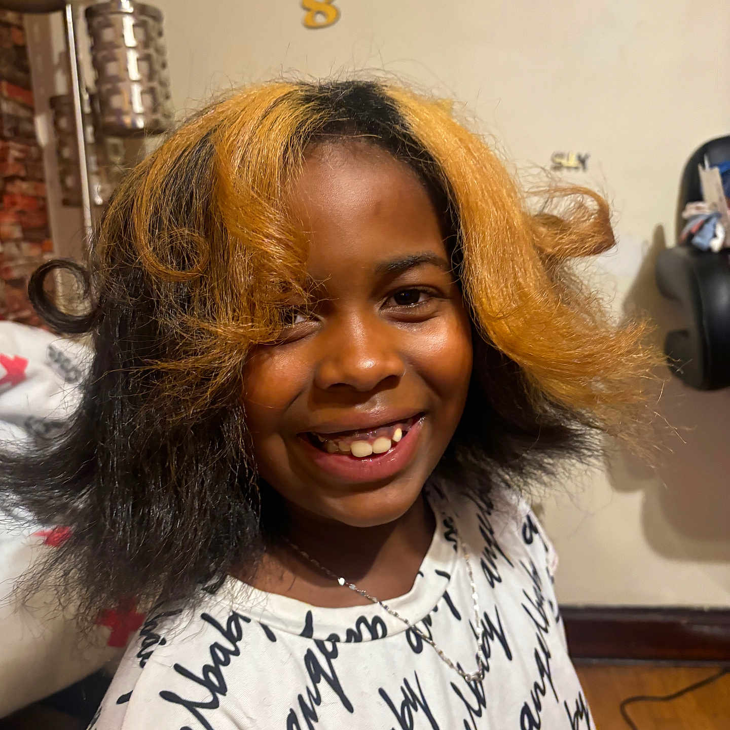 Mahraj joined the competition — help win amazing prizes! black_hair, blonde_hair, casual, chair, child, cozy, face, hair, happy, home, indoor, lamp, necklace, person, portrait, shirt, smile, text_on_clothing, two_tone_hair, wooden_floor