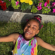 Anayiah is registered to the contest to win money with this photo: child, smiling, grass, flowers, yellow_flowers, pink_flowers, sunlight, happy, outdoor, beads, hair_accessories, colorful_clothing, tie_dye, summer, nature, portrait, relaxing, greenery, joy, closed_eyes