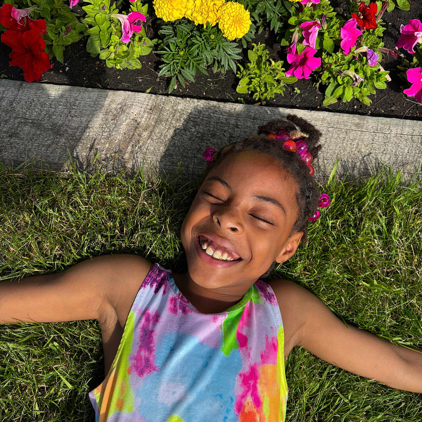 Anayiah is registered to the contest to win money with this photo: beads, child, closed_eyes, colorful_clothing, flowers, grass, greenery, hair_accessories, happy, joy, nature, outdoor, pink_flowers, portrait, relaxing, smiling, summer, sunlight, tie_dye, yellow_flowers