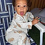 child, toddler, pajamas, animal_print, chair, lawn_chair, toy, hand, expression, surprise, outdoor, night, fence, curly_hair, footwear, striped, seating, person, clothing, face