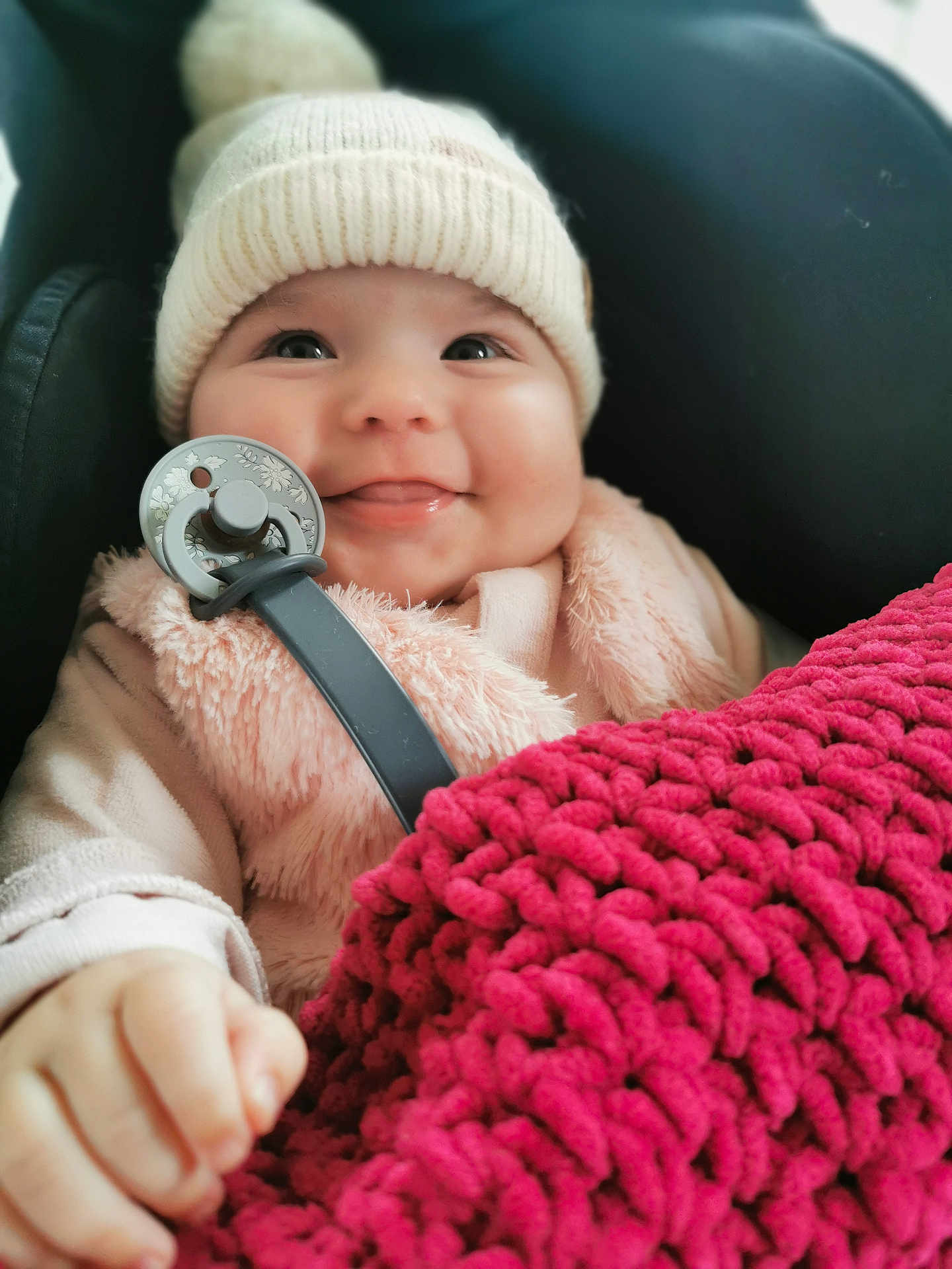 Eléna a rejoint le concours — aidez-le/la à gagner de superbes lots ! baby, smiling, hat, knit_hat, pacifier, blanket, red_blanket, fuzzy_jacket, pink_clothing, cute, infant, child, portrait, closeup, warm_clothing, cozy, happy, indoor, person, baby_hand