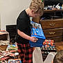child, pajamas, lego, toy_box, wrapping_paper, floor, cat, box, dresser, television, room, wooden_floor, unwrapped_presents, plaid, black_shirt, excitement, holiday, gift, indoor, person