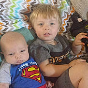 Braxton is registered to the contest to win money with this photo: baby, child, superman, batman, toy, blanket, pattern, indoor, couch, clothing, young, person, face, sitting, cute, infant, toddler, colorful, relaxed, portrait