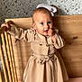 baby, bed, beige, child, coat, crib, cute, dress, finger, floral, footwear, grip, hand, indoor, infant, person, pink, standing, wallpaper, wood
