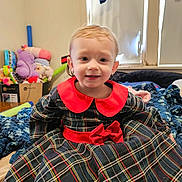 Zyla joined the competition — help win amazing prizes! toddler, child, plaid_dress, red_collar, red_bow, blanket, toys, indoor, window, curtain, smiling, face, hair, person, sitting, cozy, room, furniture, childhood, happy