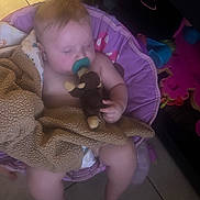Zabel is registered to the contest to win money with this photo: baby, child, pacifier, blanket, stuffed_toy, sleeping, chair, indoor, toddler, floor_tile, diaper, pink, purple, toy, cozy, cute, relaxed, soft, infant, home