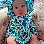 baby, child, infant, sitting, hat, blue, green, leaf_pattern, outfit, couch, floral_pattern, plush_toy, indoors, portrait, cute, chubby_cheeks, curious, soft_light, skin, person