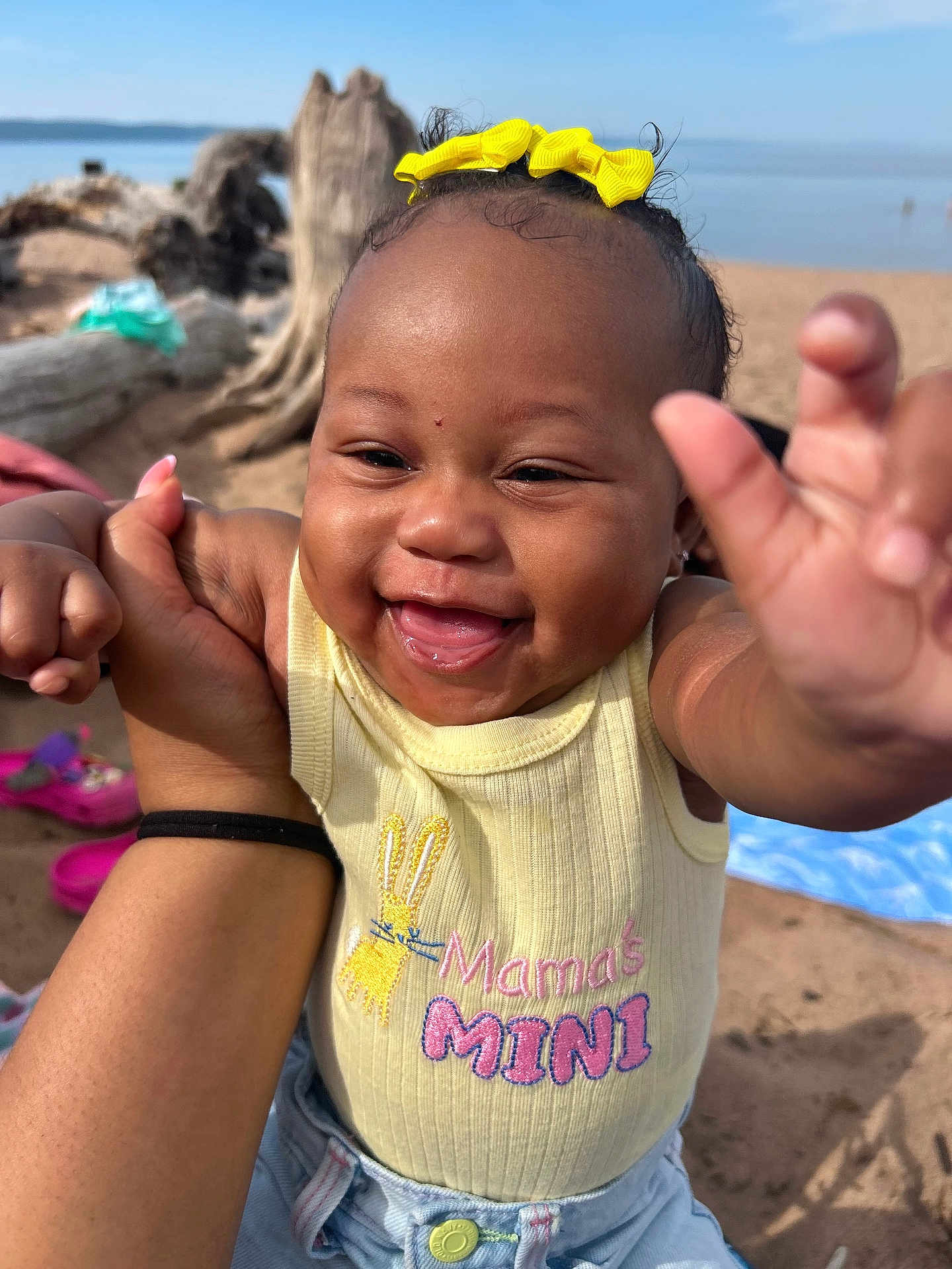 Eanaria joined the competition — help win amazing prizes! baby, child, smiling, yellow_bow, shirt, mamas_mini, hand, beach, sand, driftwood, blue_sky, outdoor, person, happy, cute, portrait, infant, reaching, denim, sunlight