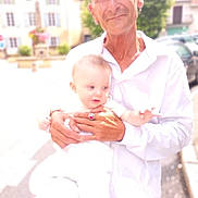 Tao participe au concours pour gagner de l'argent avec cette photo : baby, child, adult, man, person, outdoor, daylight, holding, white_clothing, street, building, blurred_background, overexposed, portrait, smile, earrings, ring, hand, face, human