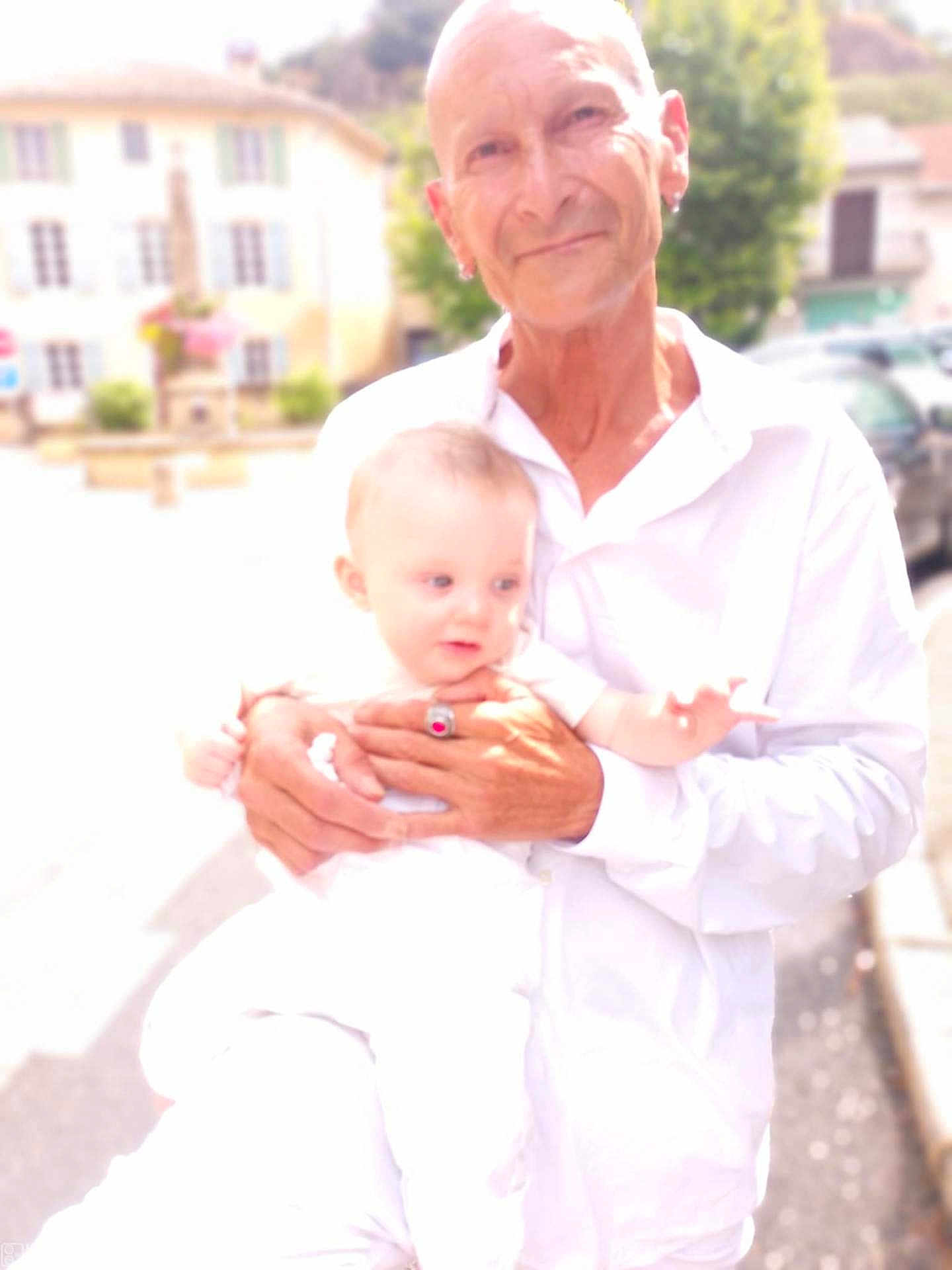 Tao participe au concours pour gagner de l'argent avec cette photo : baby, child, adult, man, person, outdoor, daylight, holding, white_clothing, street, building, blurred_background, overexposed, portrait, smile, earrings, ring, hand, face, human