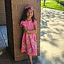 Maryfer is registered to the contest to win money with this photo: child, girl, pink_dress, bow, brick_pillar, outdoor, sidewalk, sunlight, shadow, trees, grass, smile, shoes, standing, curly_hair, casual, daylight, urban, confident, portrait