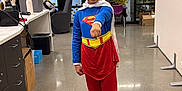 Maryfer is registered to the contest to win money with this photo: child, superhero_costume, supergirl, blue_top, red_pants, white_cape, smiling, posing, office, glass_wall, polka_dots, chair, desk, box, floor, indoor, modern, young_girl, happy, costume